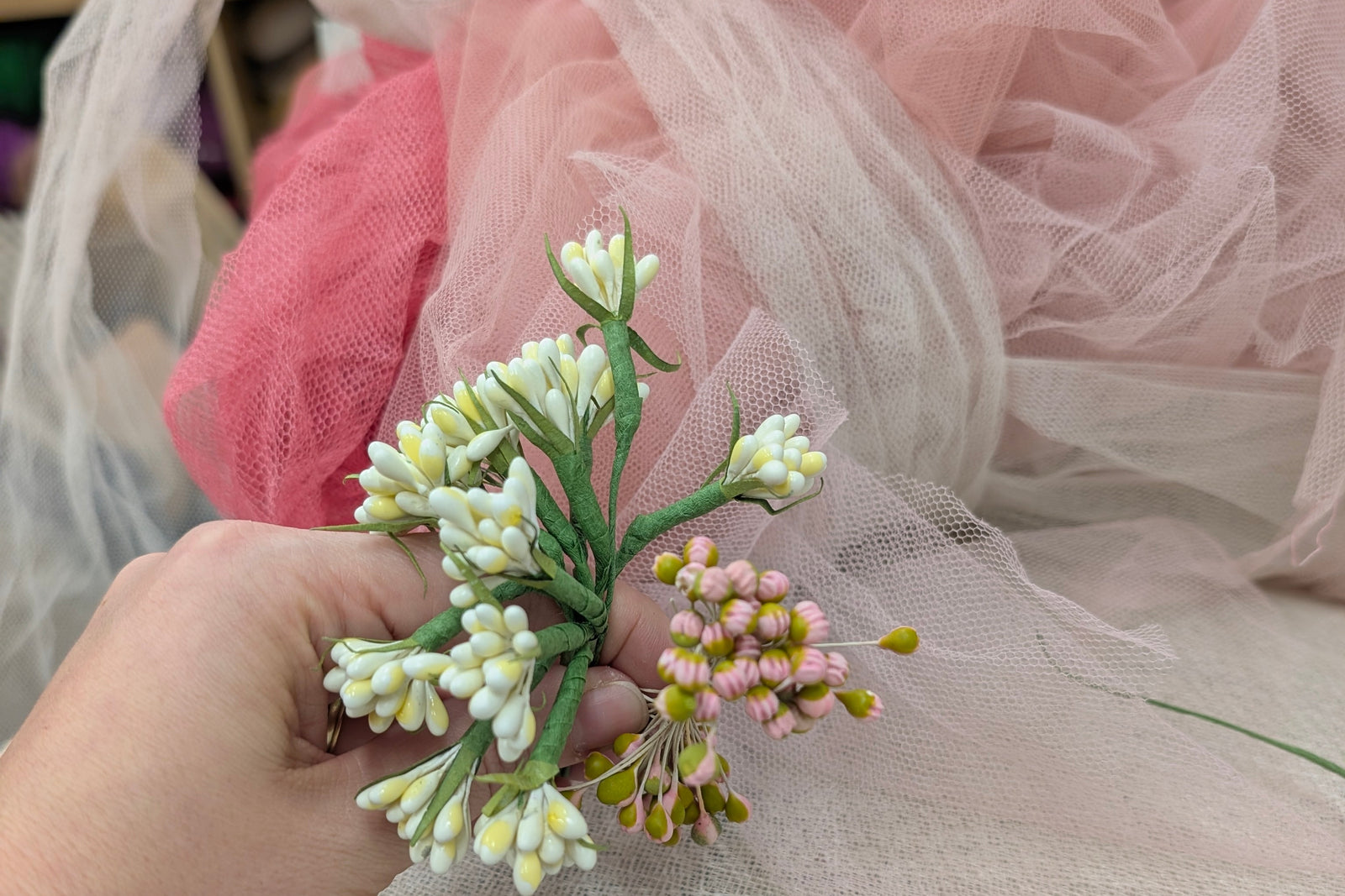 Hand holding a small bouquet of flowers with a pink and white tulle background