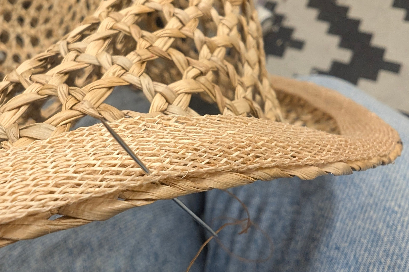 Woven straw hat on a person wearing blue jeans with a patterned rug in the background