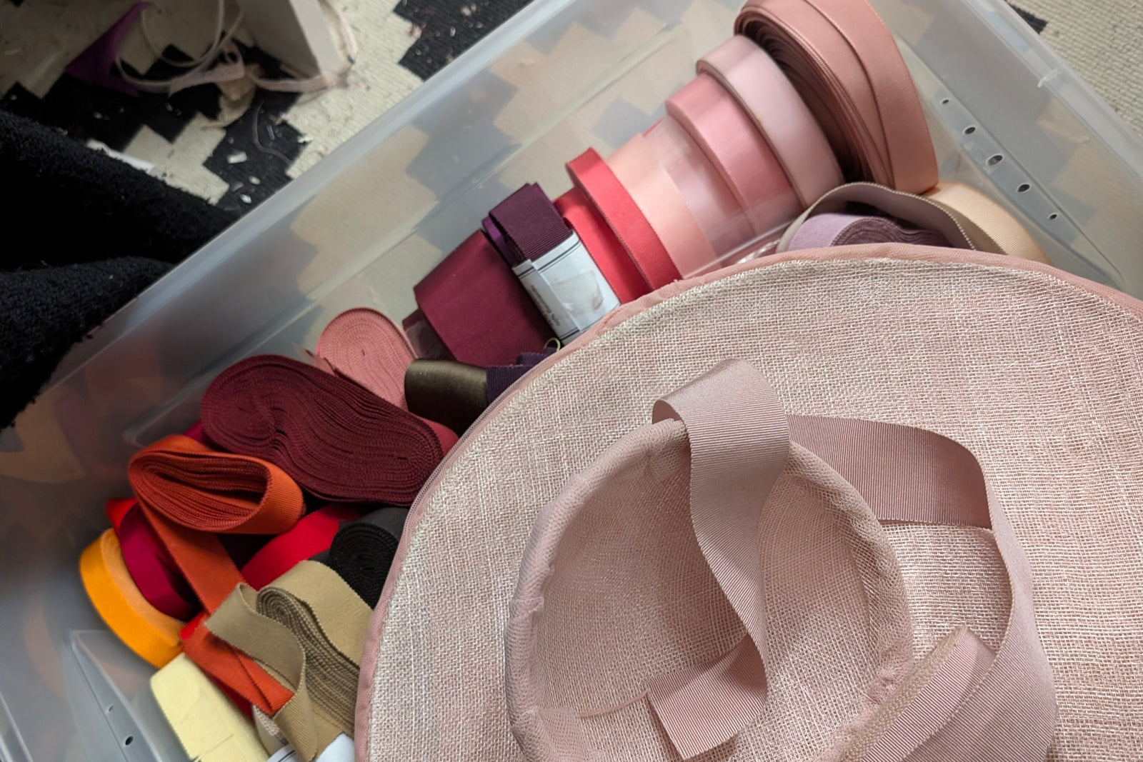 Large beige hat with ribbons on a clear plastic surface, surrounded by various colored ribbons.