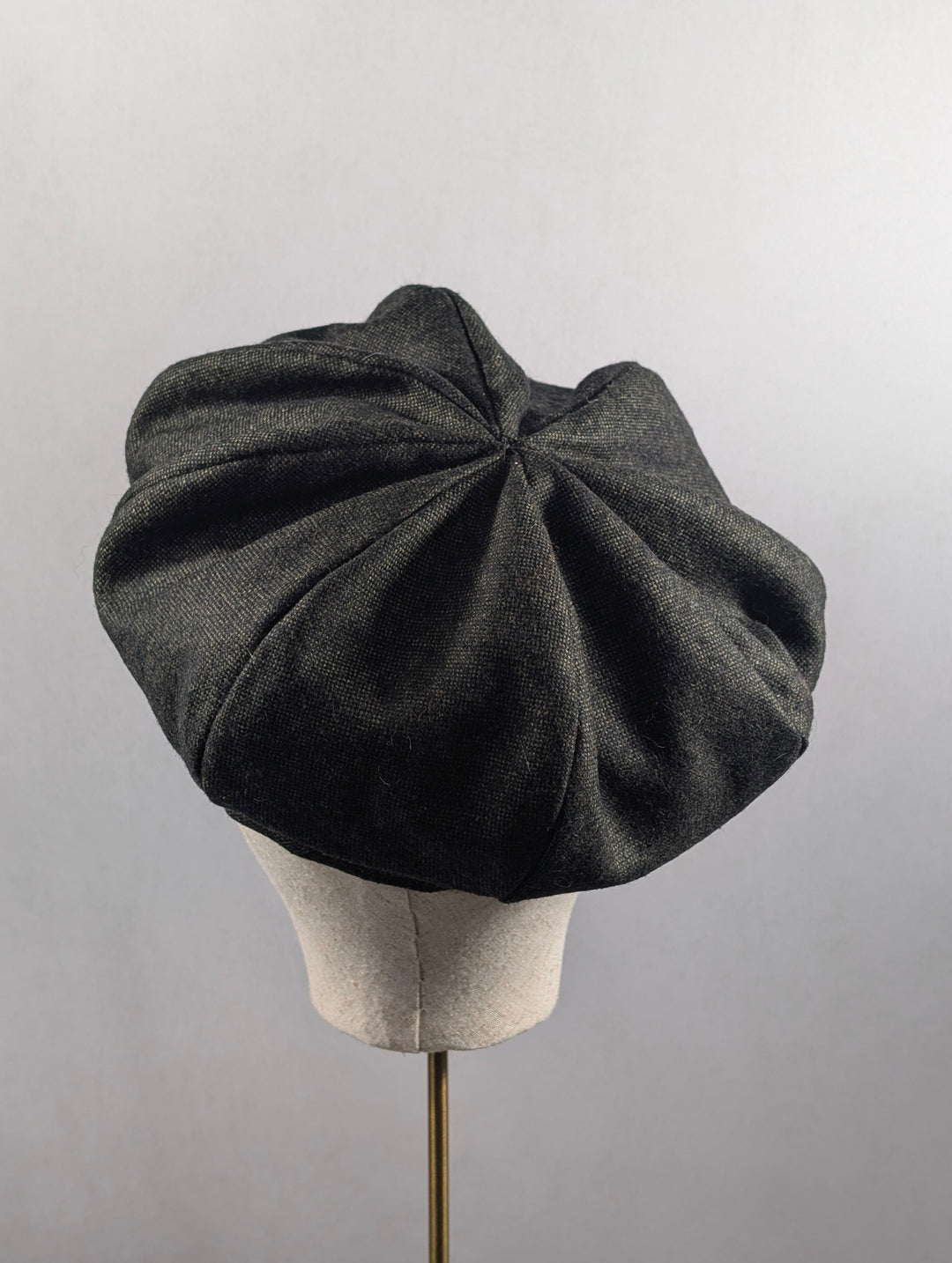 Dark gray beret on a mannequin head against a light gray background