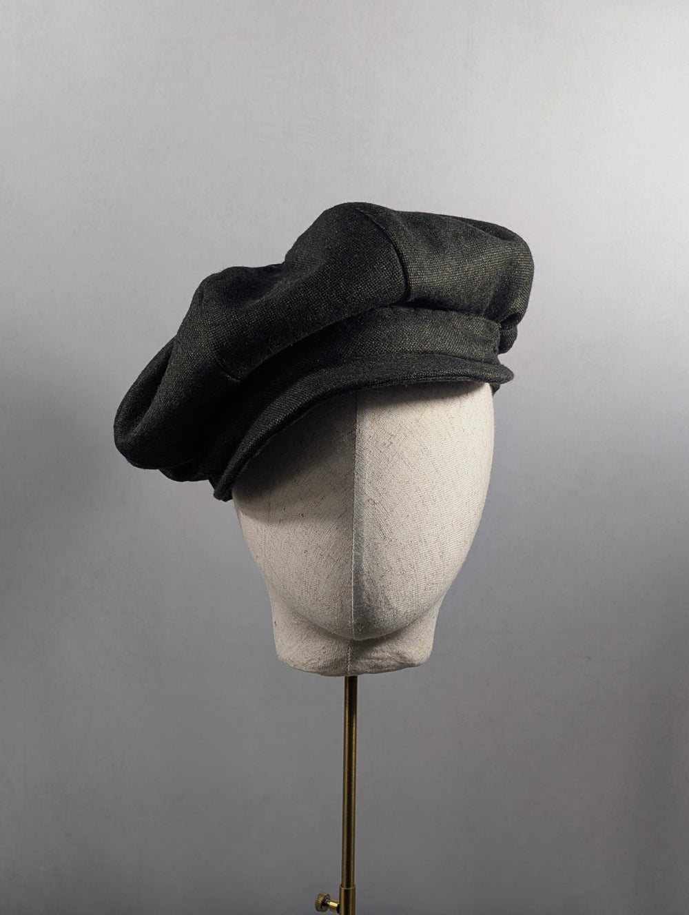 Dark gray beret on a mannequin head against a plain background