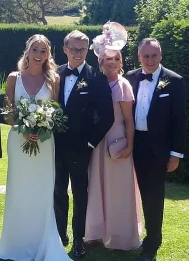 Group of four people in wedding attire standing outdoors with greenery in the background