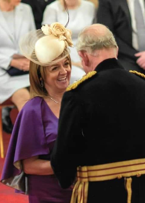 Woman in formal attire with a decorative hat interacting with a man in military uniform on a red carpet.