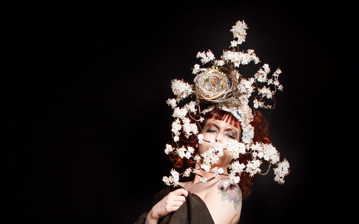 Person in traditional attire with floral headpiece against a dark background