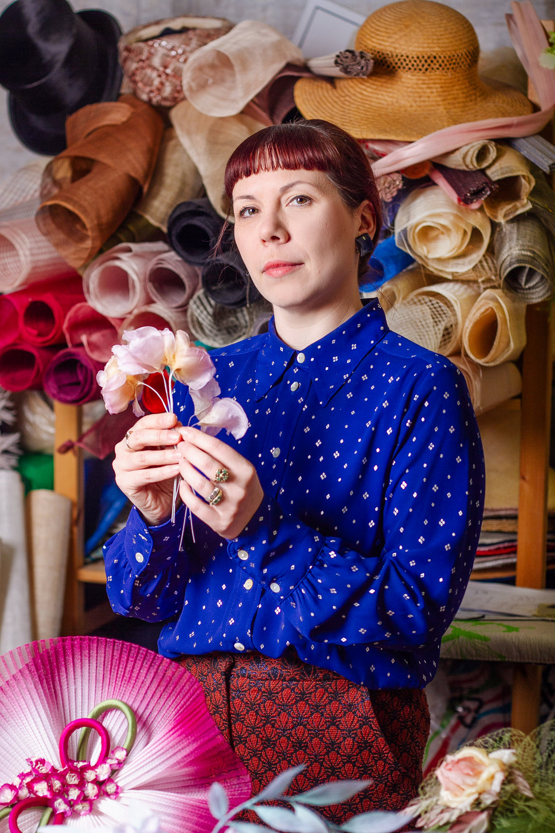 Founder and designer Giulia holding a flower in front of a colourful hat display