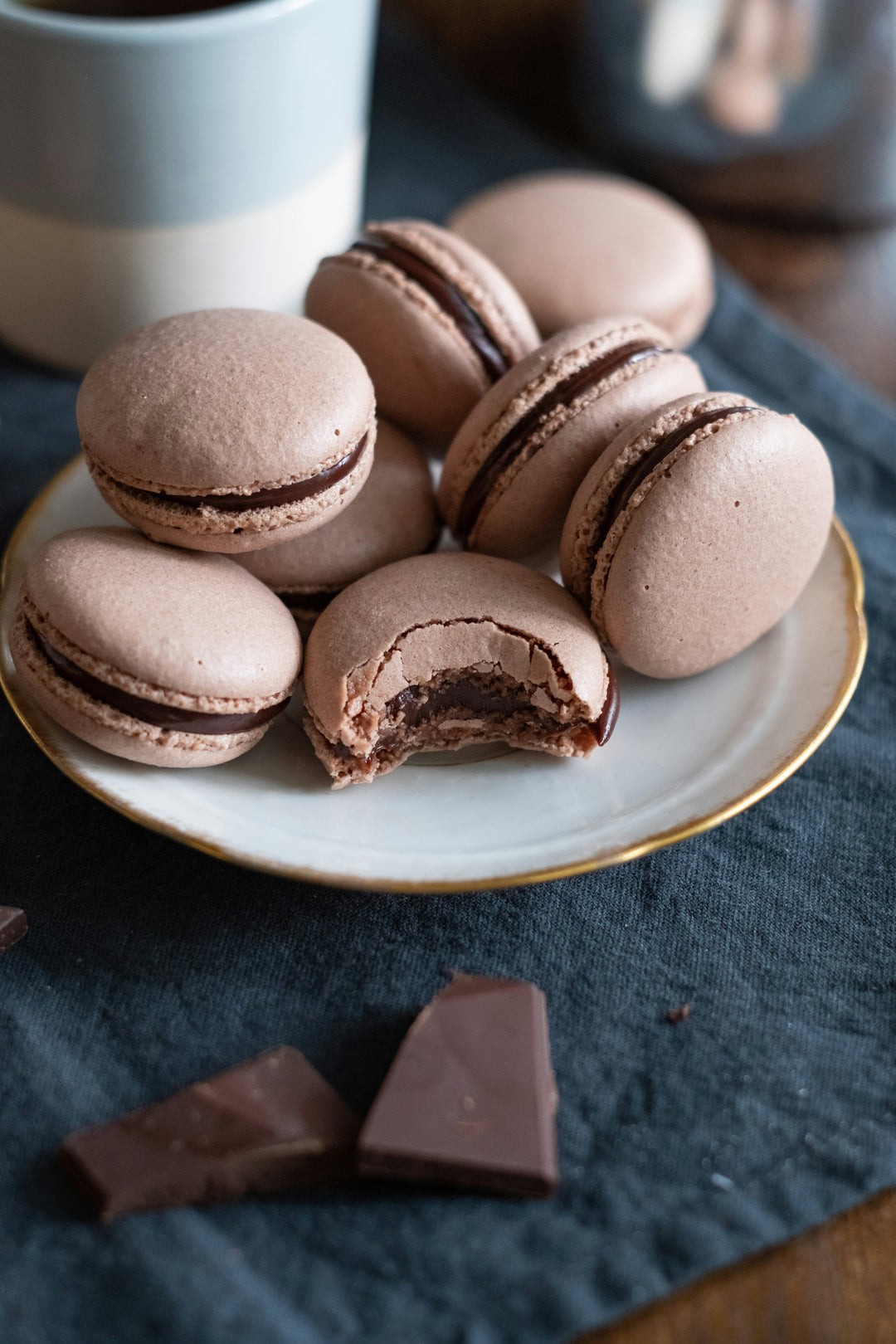 Chocolate macarons on a plate with a cup in the background