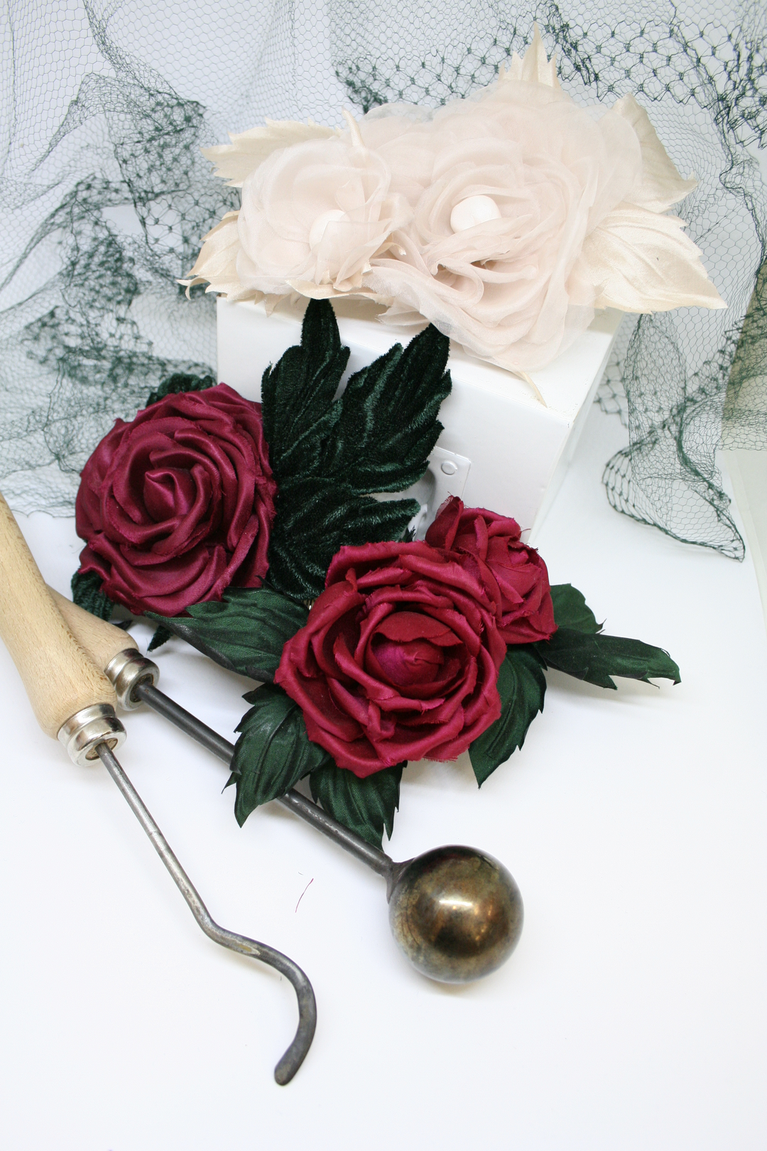 A silk rose with green leaves and red petals, created as a result of a floral workshop, displayed alongside a pair of crafting tools.