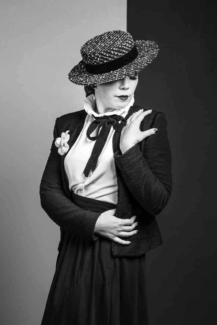 A black and white image of a woman wearing a luxurious boater hat made with 100% English Tweed, finished with a black velvet ribbon.
